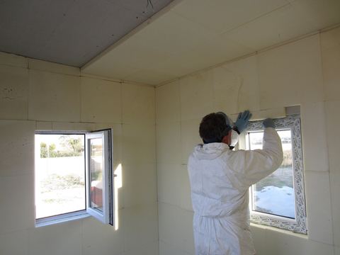 Worker in white coveralls sealing the gap around a new window set in foam insulation panels
