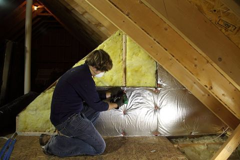 Person in a dust mask fitting insulation batts and foil facing along an attic knee wall