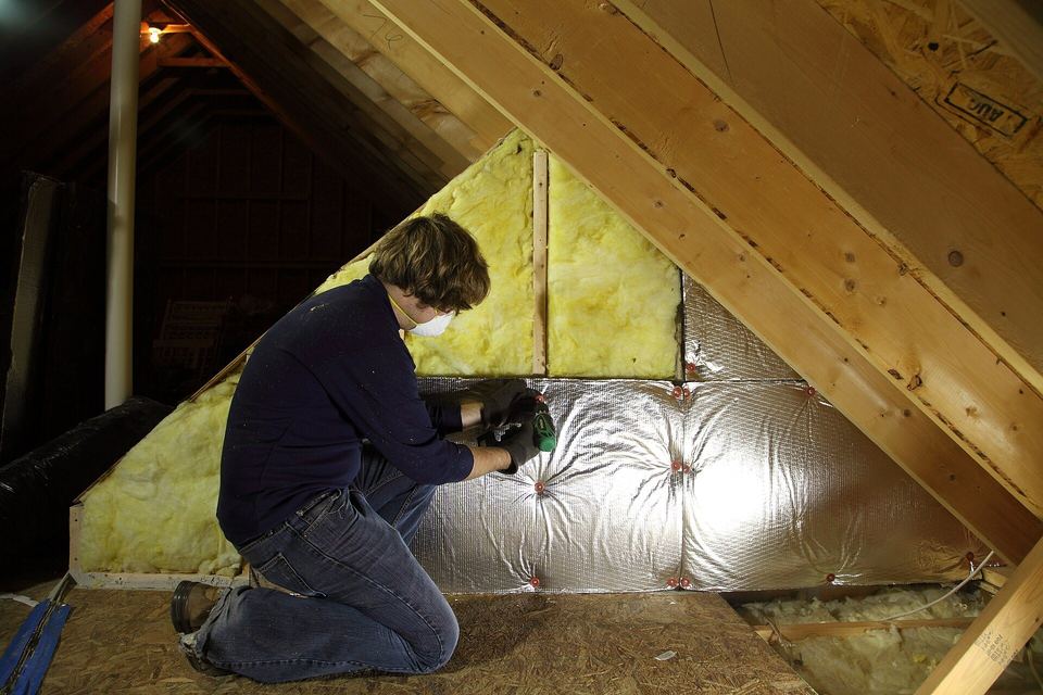 Person in a dust mask fitting insulation batts and foil facing along an attic knee wall