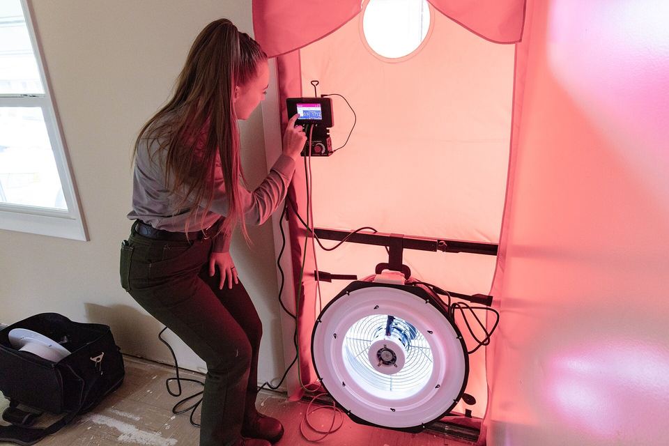 Woman reading a pressure gauge beside a blower door fan fitted in a doorway
