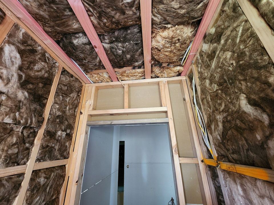 Glass-wool insulation batts fitted between wall studs and sloped ceiling framing around a doorway