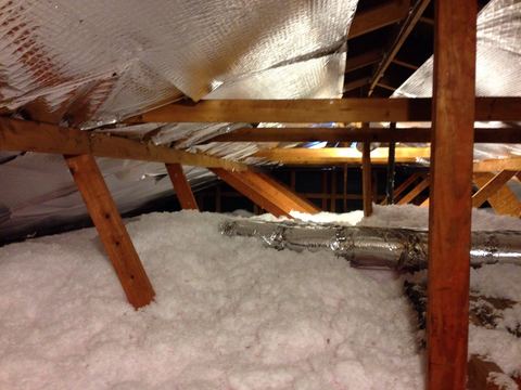 Pink loose-fill fiberglass insulation spread between attic joists beneath a foil radiant barrier and duct