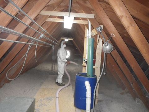 Installer in a white protective suit blowing loose-fill insulation through a hose in an attic