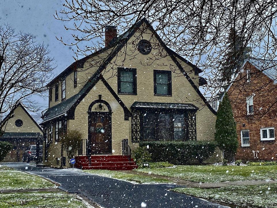 Tudor-style two-story house with a steep gabled front during a light snowfall