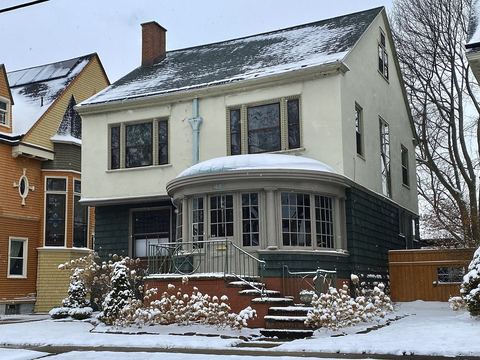 Two-story house with a rounded front porch and snow-dusted shrubs after a winter snowfall