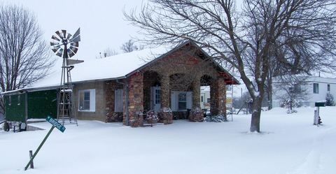 Stone-pillared bungalow with a snow-covered yard, bare trees and a windmill in winter