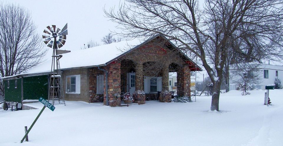 Stone-pillared bungalow with a snow-covered yard, bare trees and a windmill in winter